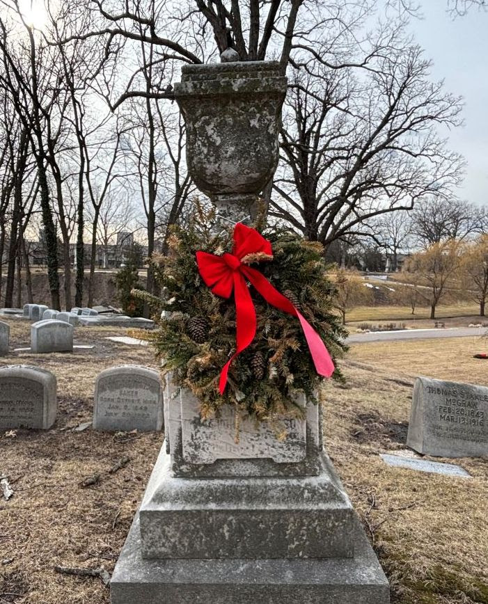 an old marble monument at a cemetery, decorated with an evergreen wreath and a red ribbon